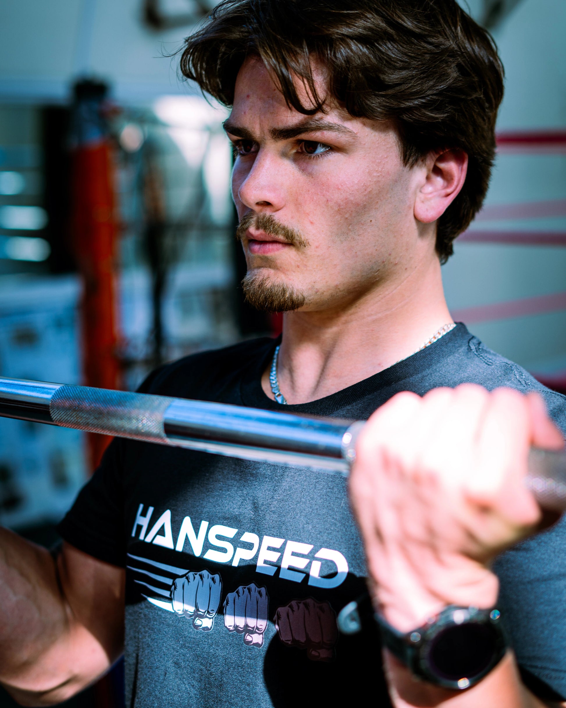 Man lifting a barbell with 'Hanspeed' shirt in gym setting