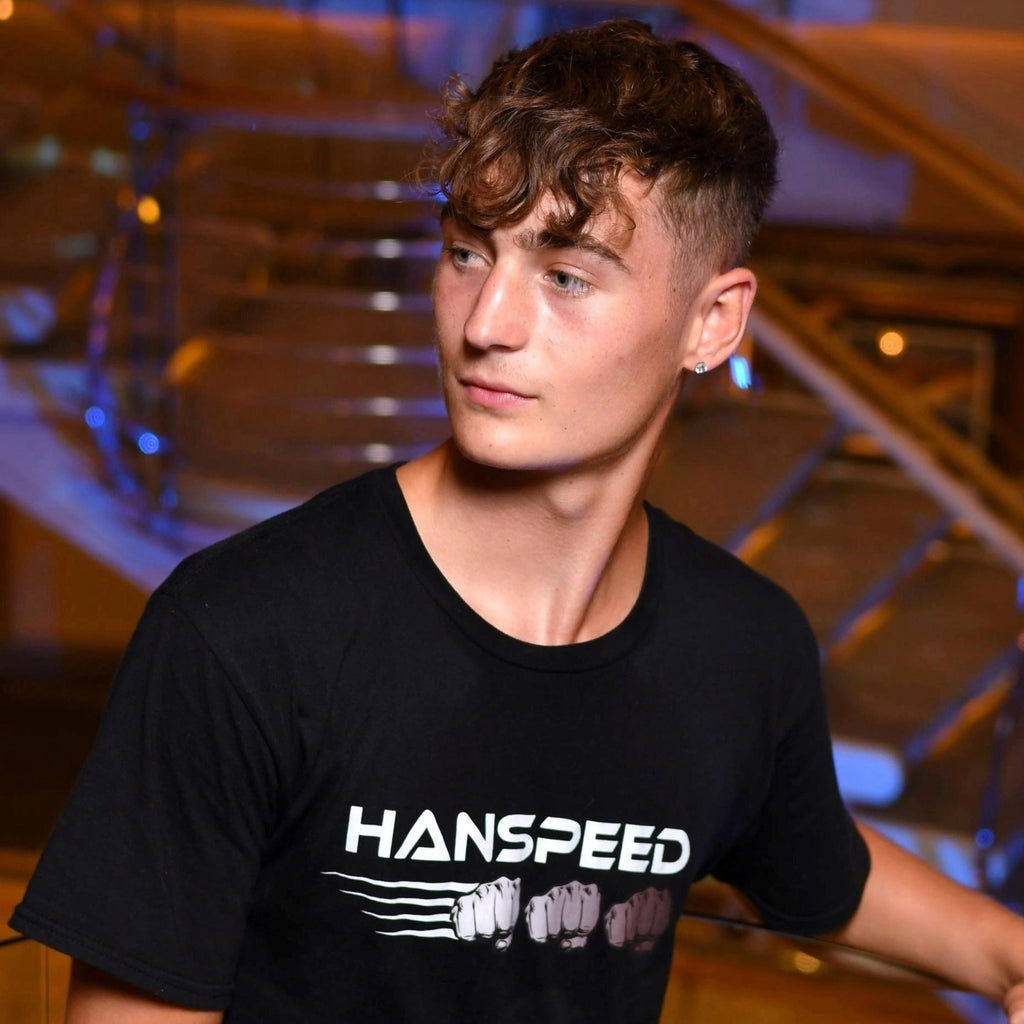 Person wearing a black 'HANSPEED' t-shirt in an indoor setting with architectural elements.