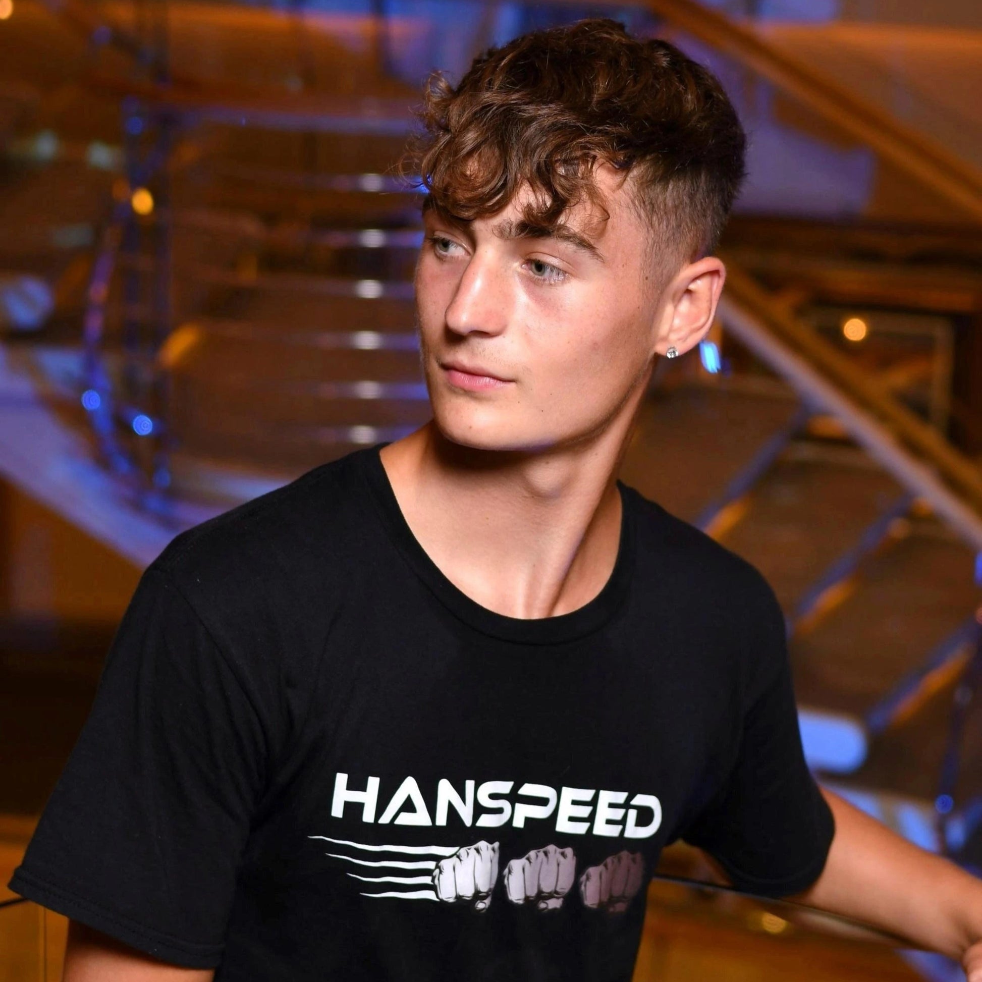 Person wearing a black 'HANSPEED' t-shirt in an indoor setting with architectural elements.